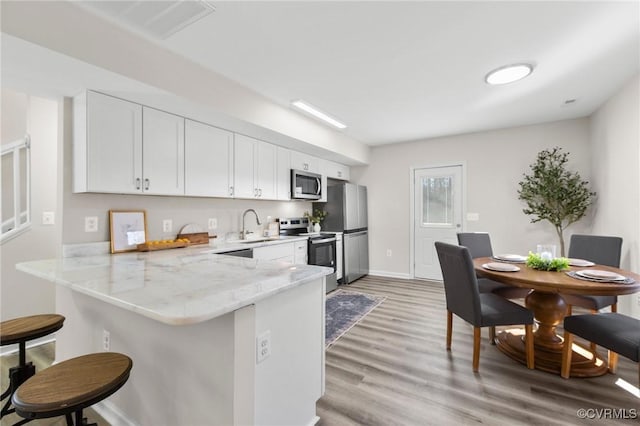 kitchen featuring a kitchen breakfast bar, white cabinets, light wood-style floors, appliances with stainless steel finishes, and a sink