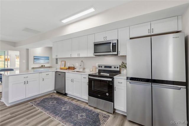 kitchen with white cabinets, light countertops, light wood-type flooring, a peninsula, and stainless steel appliances