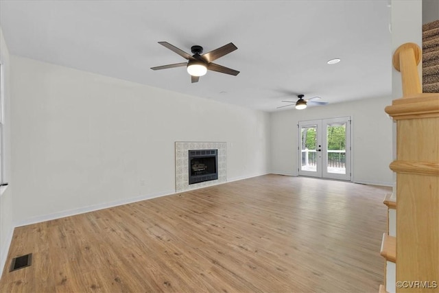 unfurnished living room with a tiled fireplace, a ceiling fan, wood finished floors, and visible vents