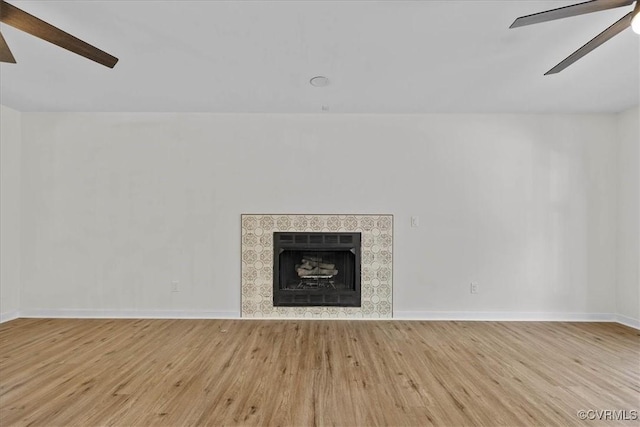 unfurnished living room with a ceiling fan, baseboards, wood finished floors, and a fireplace