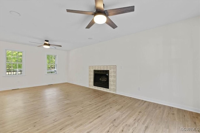 unfurnished living room featuring light wood-style floors, baseboards, ceiling fan, and a tile fireplace