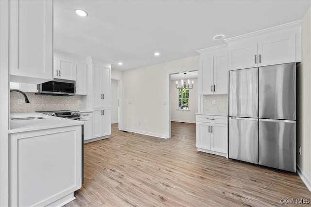kitchen featuring white cabinets, a sink, light wood-style floors, a chandelier, and stainless steel appliances