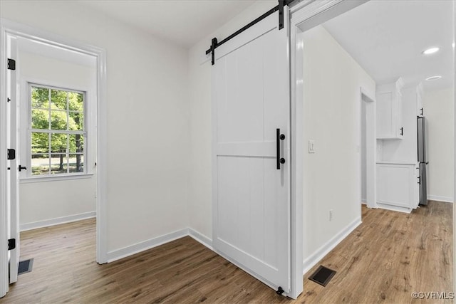 hall featuring baseboards, visible vents, a barn door, and wood finished floors