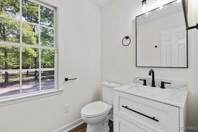 half bathroom featuring plenty of natural light, wood finished floors, toilet, and vanity