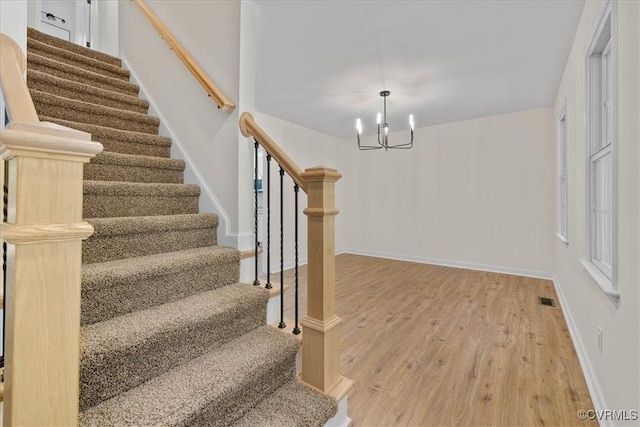 stairs featuring baseboards, a notable chandelier, wood finished floors, and visible vents