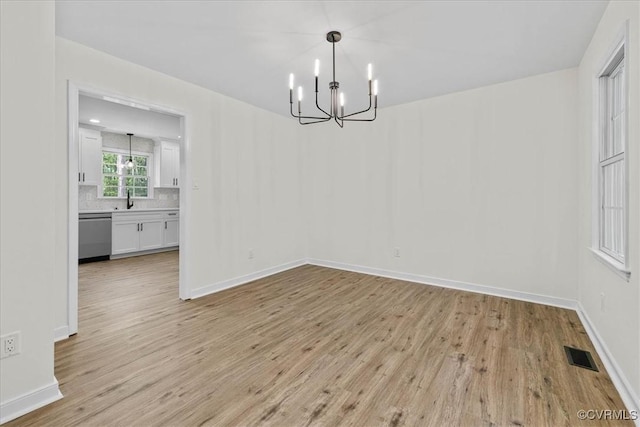 unfurnished dining area featuring visible vents, a sink, baseboards, a notable chandelier, and light wood-style floors