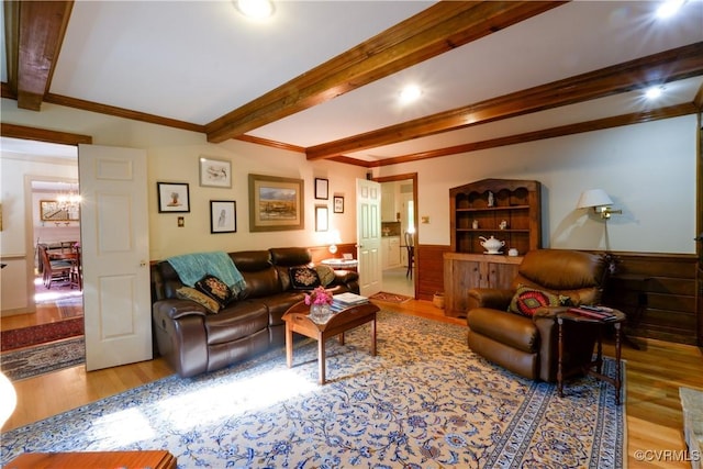 living room with a chandelier, a wainscoted wall, wood finished floors, beamed ceiling, and ornamental molding