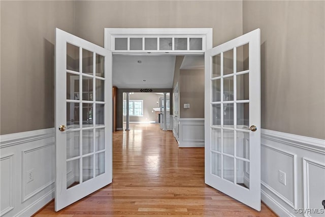 hallway with wood finished floors, wainscoting, french doors, and a decorative wall