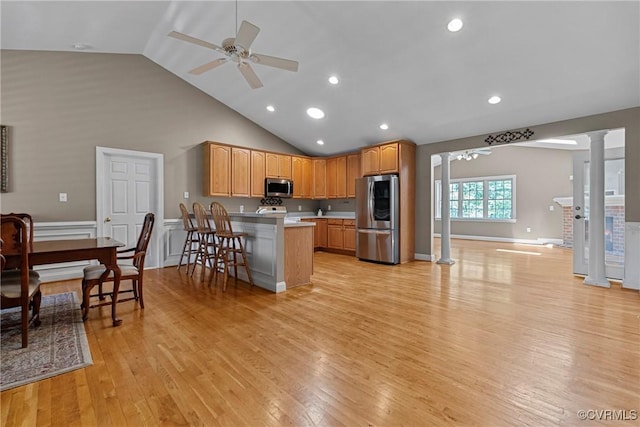 kitchen with decorative columns, a peninsula, light wood-type flooring, a ceiling fan, and stainless steel appliances