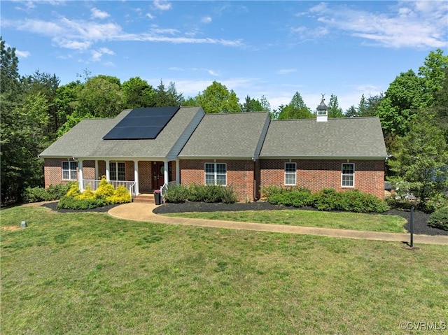 ranch-style home featuring a porch, brick siding, solar panels, and a front lawn