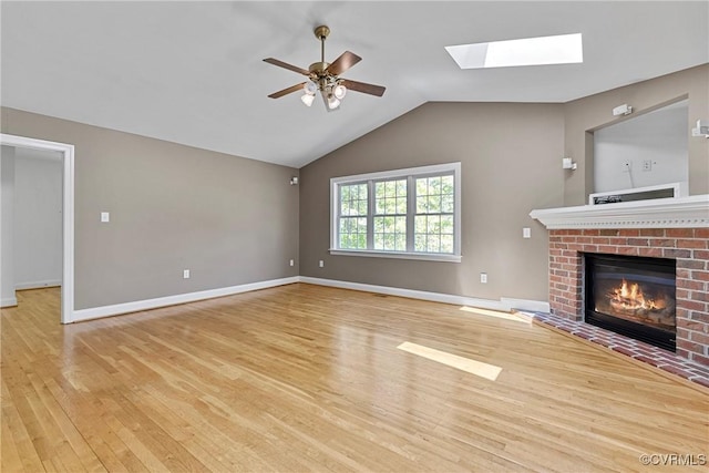 unfurnished living room with a brick fireplace, a ceiling fan, baseboards, wood finished floors, and lofted ceiling with skylight