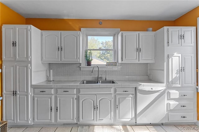 kitchen featuring tile countertops, dishwasher, a sink, and white cabinets