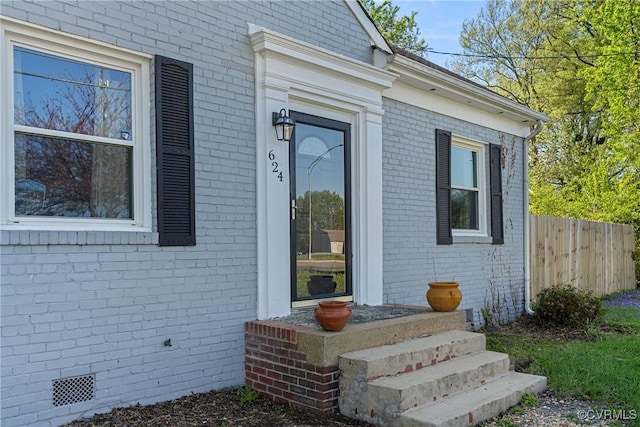 property entrance with crawl space, fence, and brick siding