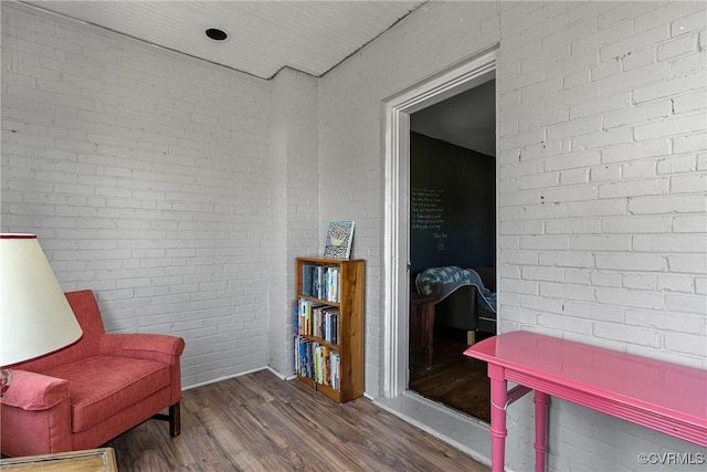 sitting room with brick wall and dark wood finished floors