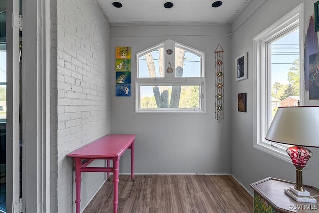 doorway to outside with wood finished floors, brick wall, ornamental molding, and baseboards