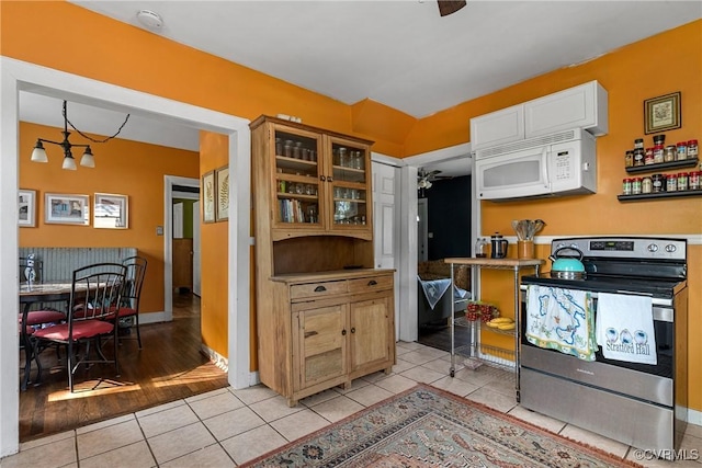 kitchen featuring white microwave, glass insert cabinets, white cabinetry, stainless steel range with electric stovetop, and light tile patterned flooring