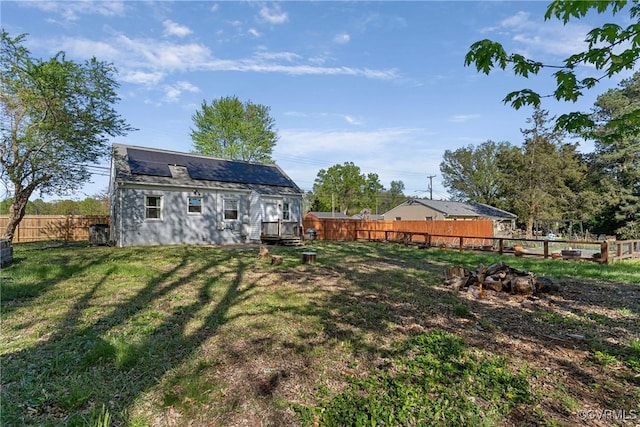 rear view of property with a fenced backyard, a lawn, and roof mounted solar panels