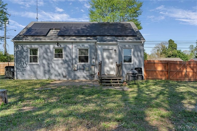 rear view of house featuring a yard, fence, and roof mounted solar panels