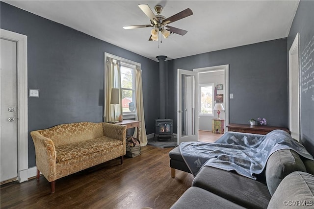 bedroom with a wood stove, multiple windows, wood finished floors, and a ceiling fan