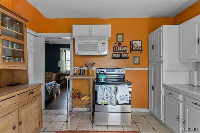 kitchen featuring white microwave, light tile patterned floors, glass insert cabinets, white cabinetry, and stainless steel electric range
