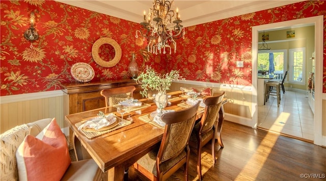 dining space with an inviting chandelier, wainscoting, wallpapered walls, and wood finished floors