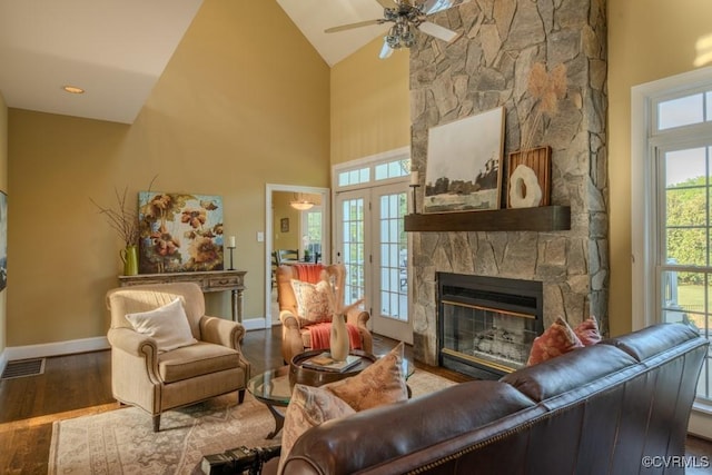 living area featuring visible vents, wood finished floors, a stone fireplace, baseboards, and a ceiling fan