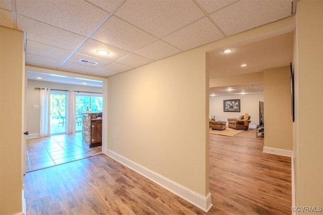 hallway with a paneled ceiling, baseboards, visible vents, and wood finished floors