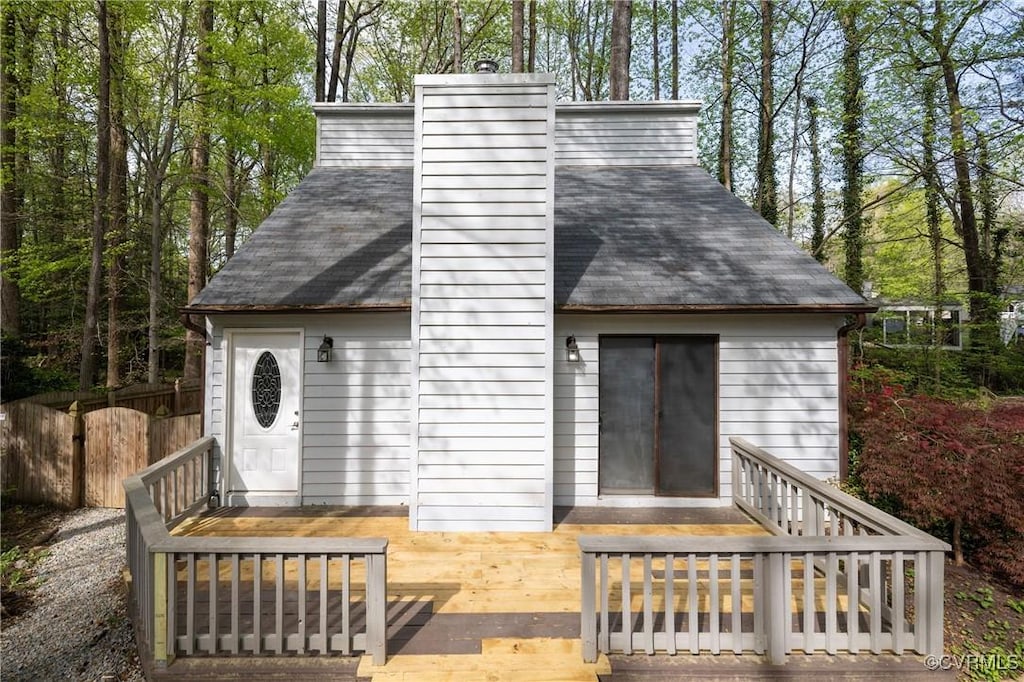 back of house with fence, a shingled roof, a deck, and a chimney