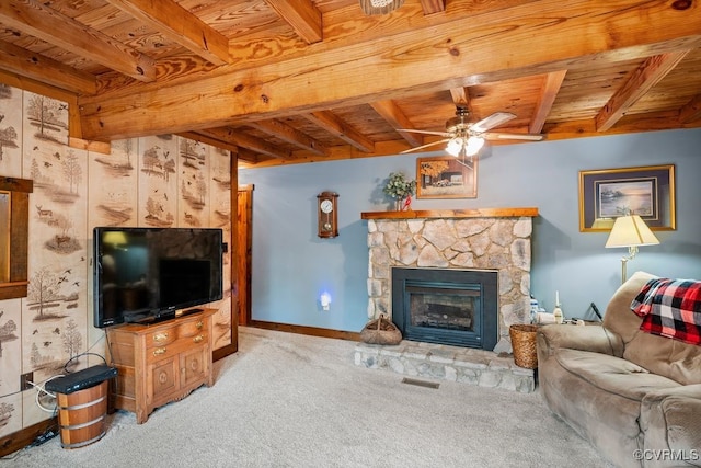 carpeted living area with beamed ceiling, a stone fireplace, a ceiling fan, and wood ceiling