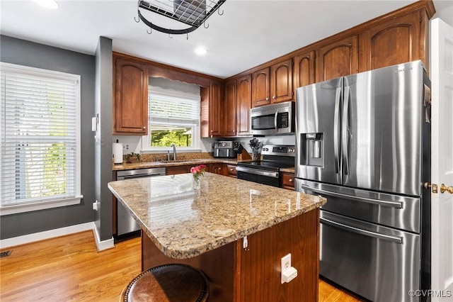 kitchen with light stone countertops, appliances with stainless steel finishes, light wood-style floors, baseboards, and a kitchen island