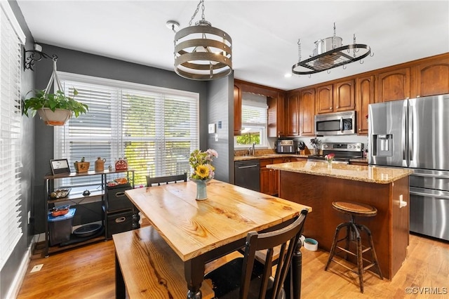 kitchen featuring light stone counters, a sink, light wood-style flooring, a center island, and stainless steel appliances