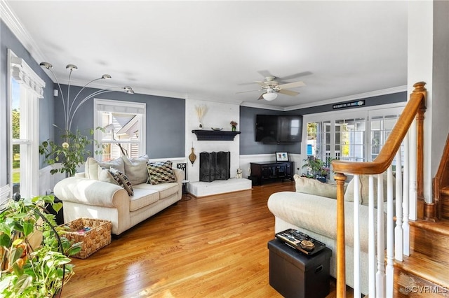 living area featuring ceiling fan, light wood-style floors, a fireplace with raised hearth, ornamental molding, and stairway