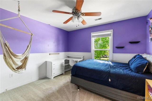 carpeted bedroom featuring a ceiling fan, wood walls, visible vents, and a wainscoted wall