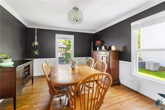 dining area featuring light wood-type flooring, ornamental molding, and a wainscoted wall