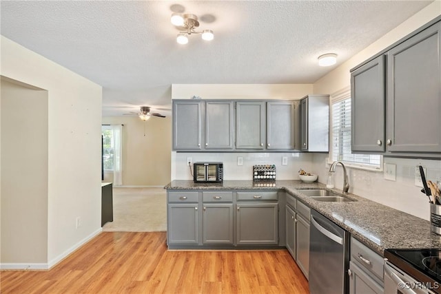 kitchen with appliances with stainless steel finishes, a sink, a textured ceiling, gray cabinets, and light wood-type flooring