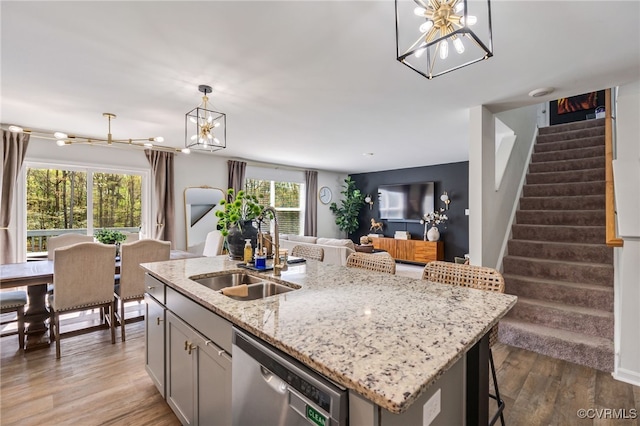 kitchen with wood finished floors, a sink, open floor plan, dishwasher, and an inviting chandelier