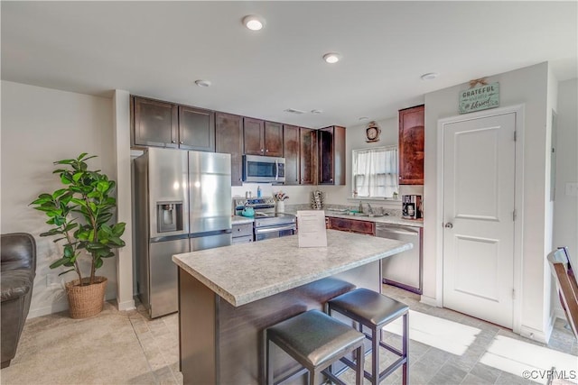 kitchen featuring a sink, a kitchen breakfast bar, a kitchen island, light countertops, and appliances with stainless steel finishes