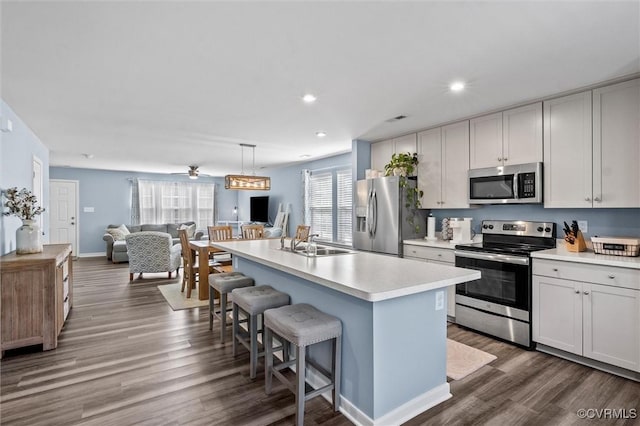 kitchen with open floor plan, a kitchen bar, dark wood-type flooring, a sink, and appliances with stainless steel finishes