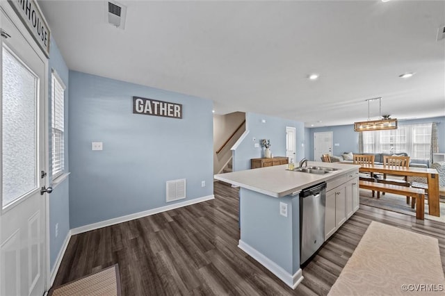 kitchen featuring stainless steel dishwasher, a sink, light countertops, dark wood-type flooring, and an island with sink
