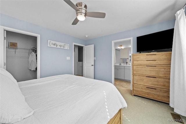 bedroom with connected bathroom, a ceiling fan, light colored carpet, and a spacious closet