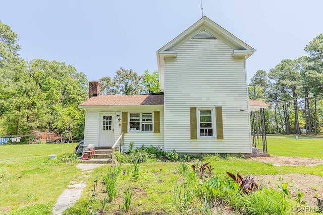 rear view of property featuring a yard, entry steps, a chimney, and a shingled roof