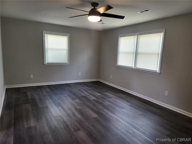spare room with dark wood finished floors, visible vents, baseboards, and ceiling fan