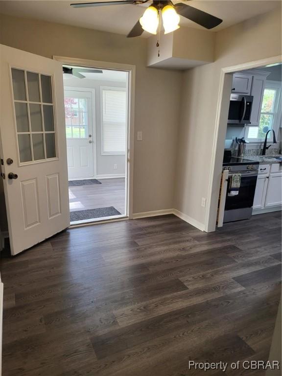 unfurnished dining area with dark wood finished floors, a sink, a ceiling fan, and baseboards
