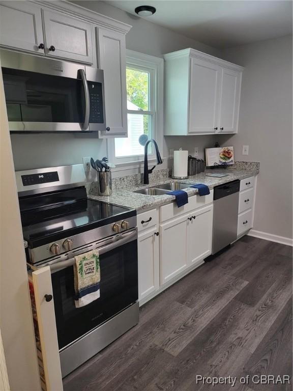 kitchen with light stone countertops, white cabinetry, appliances with stainless steel finishes, dark wood-style flooring, and a sink