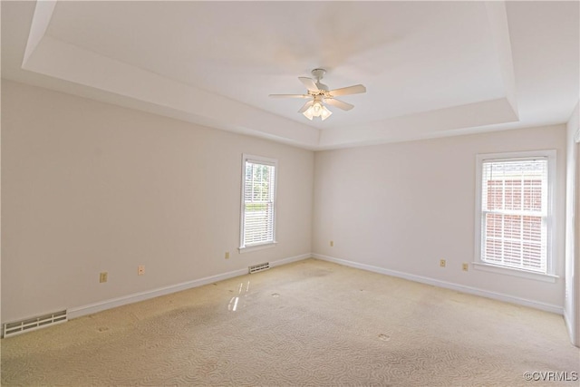spare room with ceiling fan, light colored carpet, baseboards, a tray ceiling, and visible vents