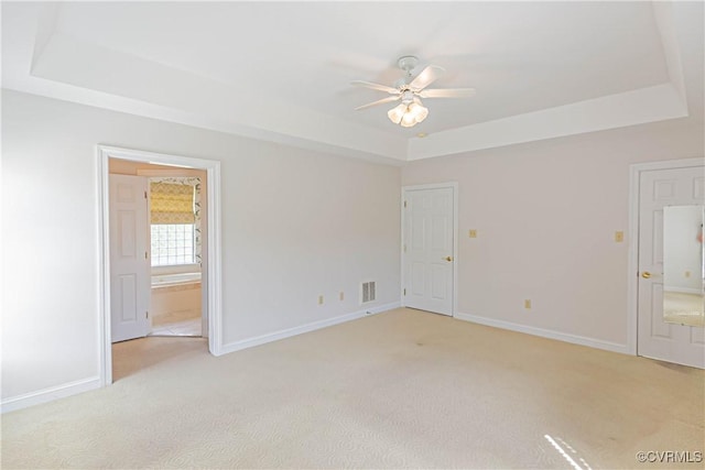 empty room featuring ceiling fan, visible vents, baseboards, light carpet, and a tray ceiling