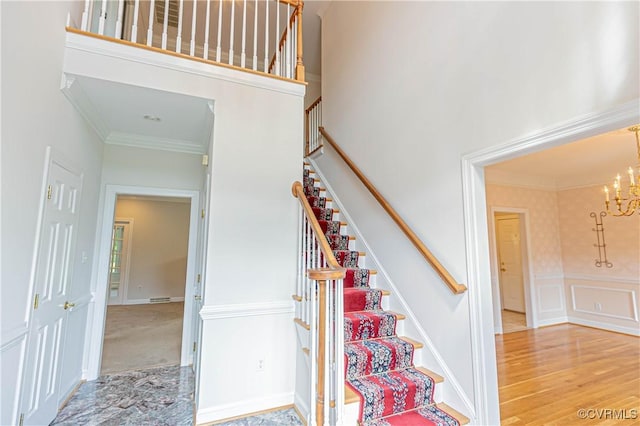 staircase featuring visible vents, ornamental molding, a towering ceiling, a decorative wall, and a chandelier