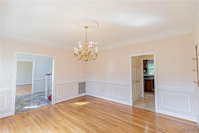 unfurnished dining area featuring visible vents, crown molding, a notable chandelier, light wood-style floors, and a decorative wall