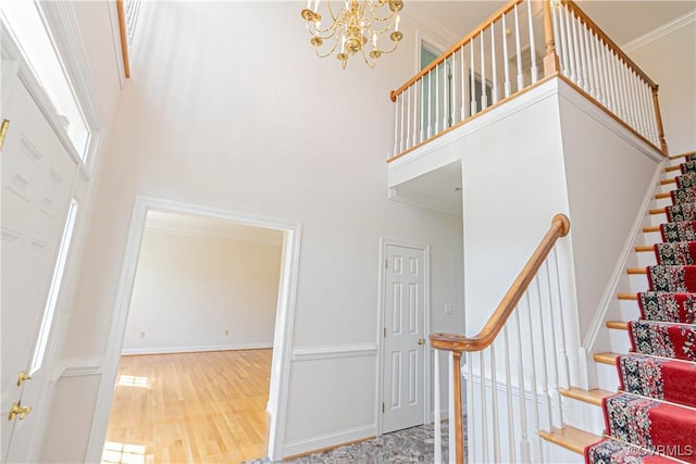 staircase featuring baseboards, a notable chandelier, wood finished floors, and a towering ceiling