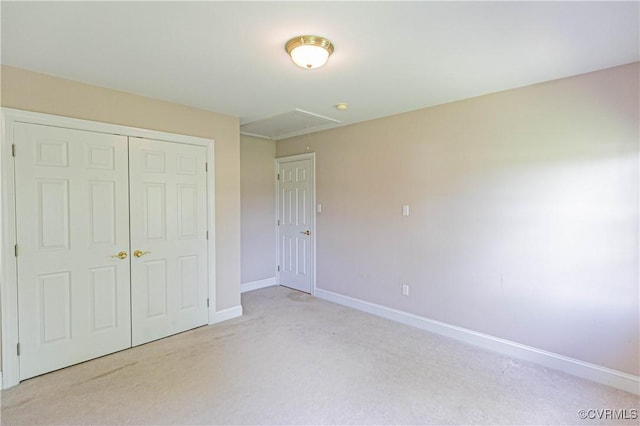 unfurnished bedroom featuring baseboards, light carpet, attic access, and a closet